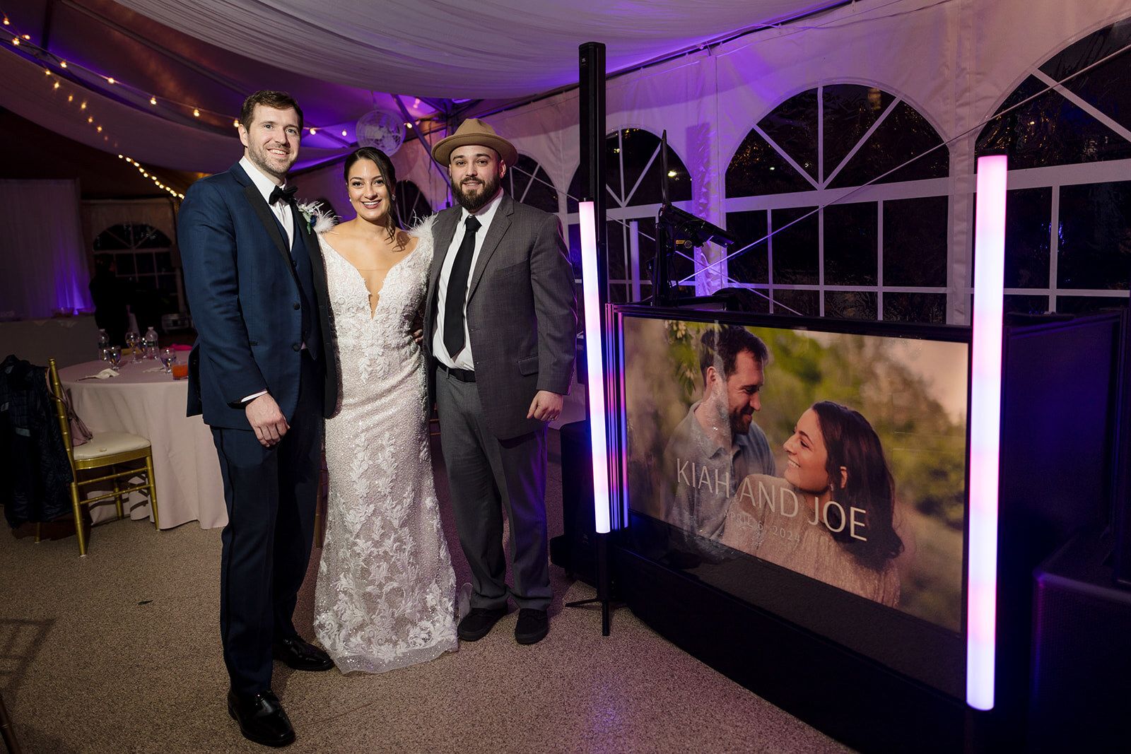 Joshua Pelling stands with a bride and groom beside their personalized Love & Light Entertainment DJ booth at a wedding reception.