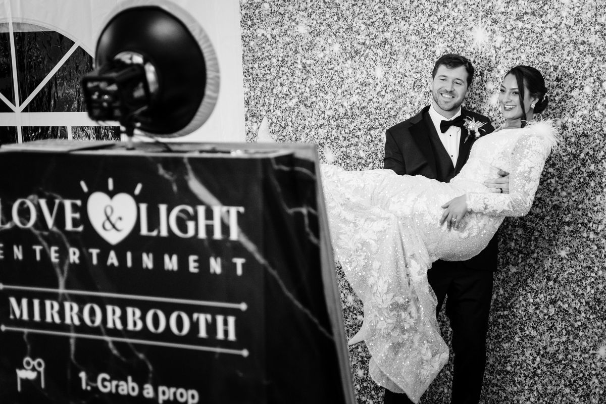 Wedding guests posing in front of the Love & Light Entertainment MirrorBooth at a reception.